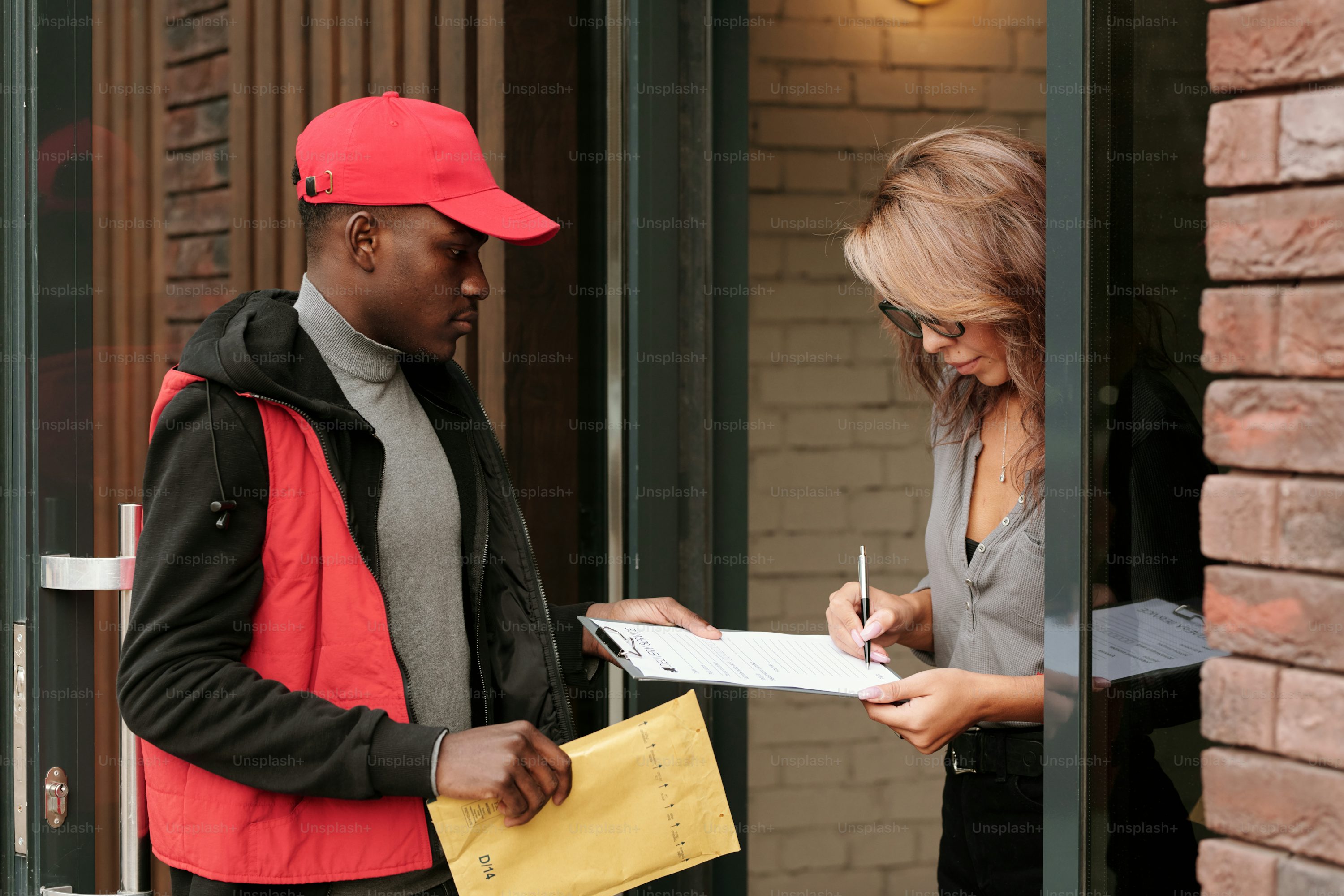 A professional process server in a red hat delivering legal documents to a resident in Fresno, California as she signs a clipboard form" 